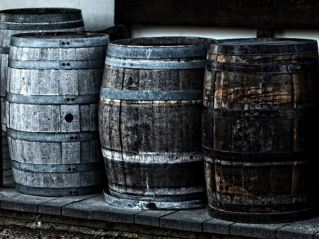 Stacked dark wooden barrels with metal hoops, weathered wood finish.