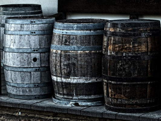 Stacked dark wooden barrels with metal hoops, weathered wood finish.
