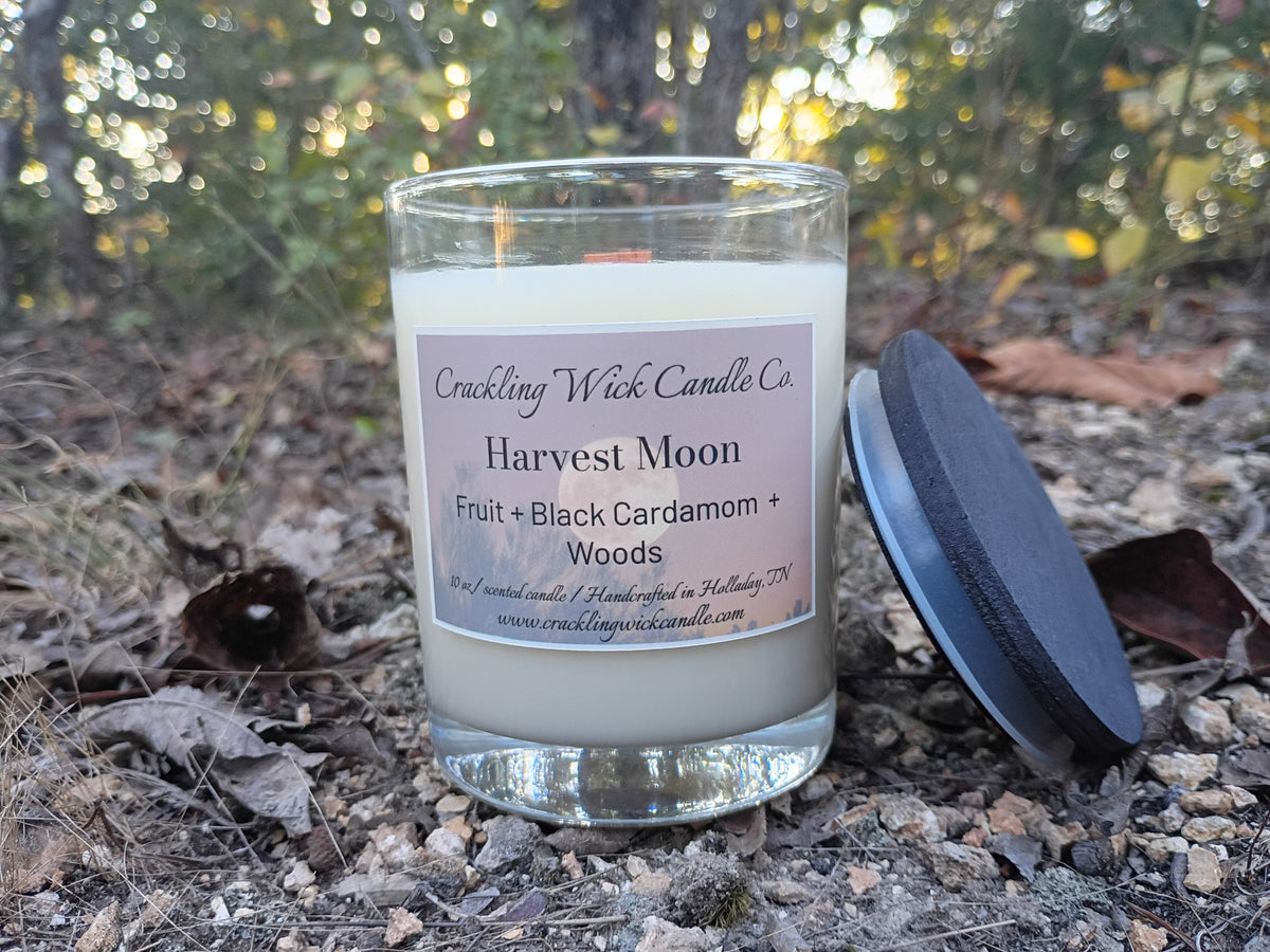 Glass jar candle with cream wax and wooden wick, black lid tilted nearby