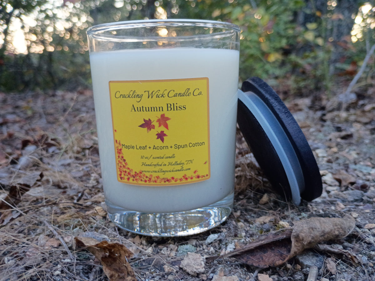 White wax candle in clear glass jar with autumn label, wick centered in glass top.