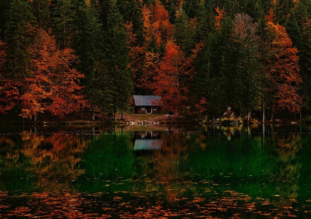 Scented candle scene with autumn forest cabin and lake reflections