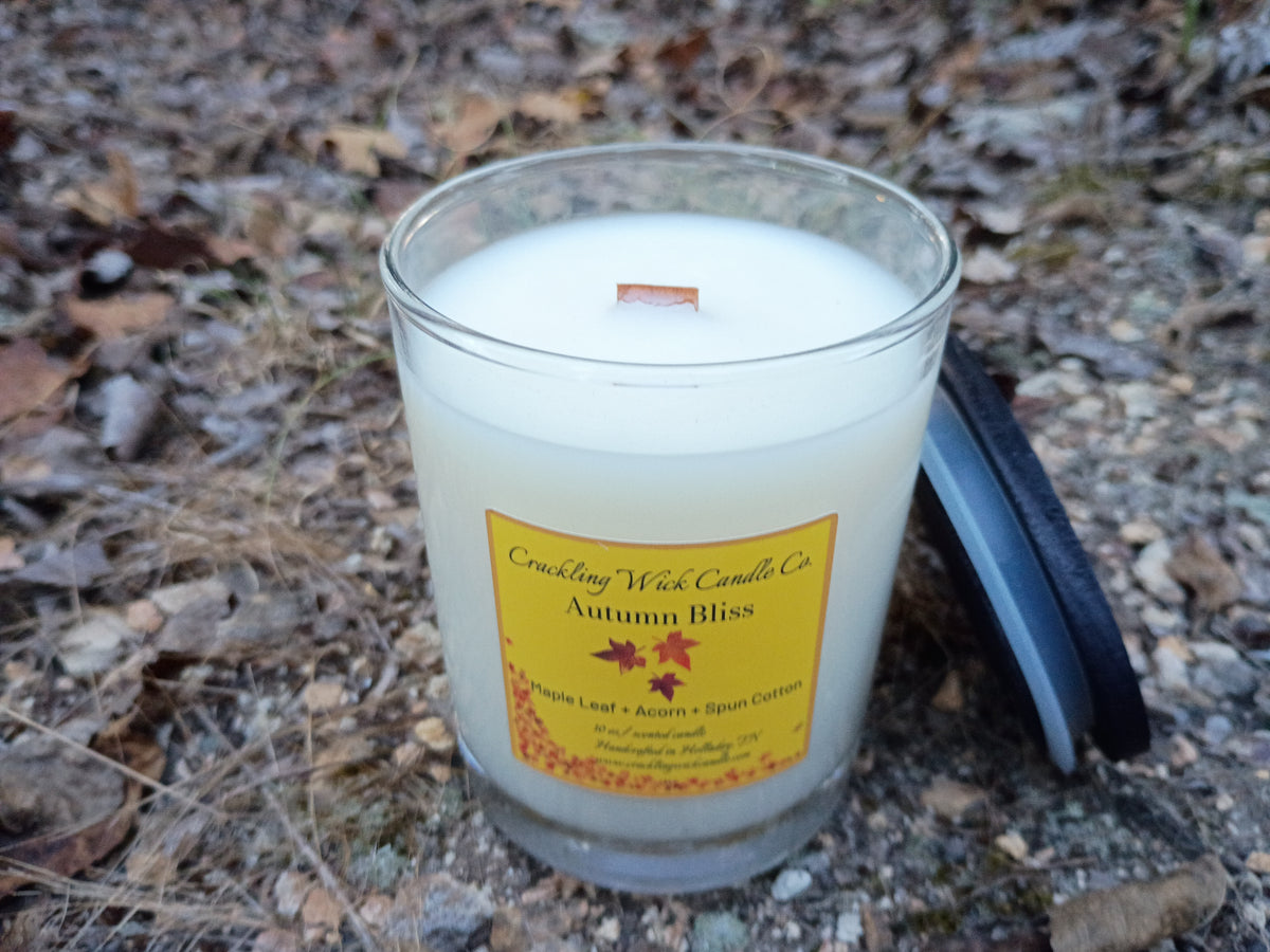 White wax candle in clear glass jar with printed autumn label, single wick visible.