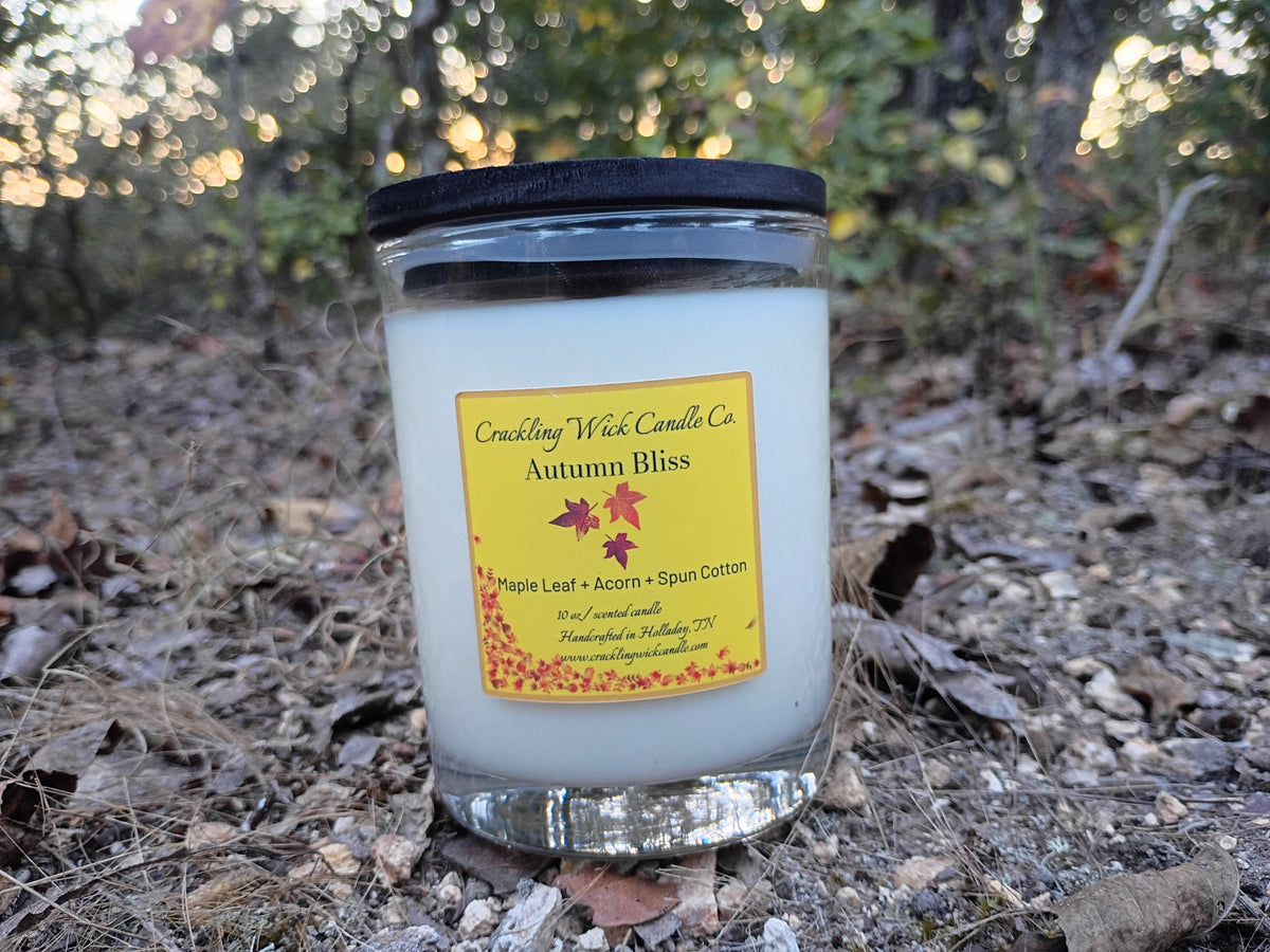 Lidded candle in clear glass jar with white wax and autumn-themed label.